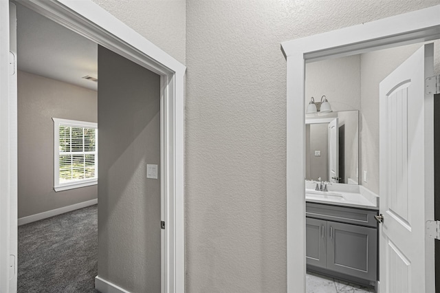 bathroom featuring visible vents, vanity, baseboards, and a textured wall