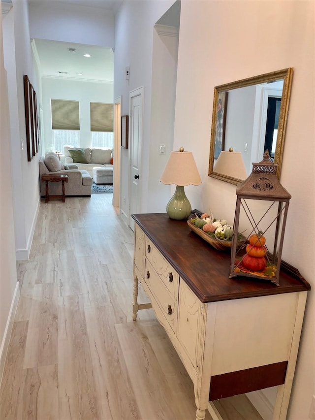 hall featuring light wood-style flooring, baseboards, and ornamental molding