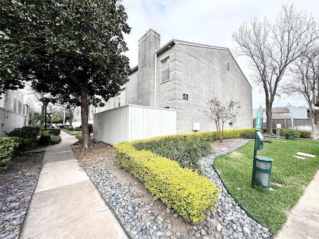 view of property exterior featuring brick siding, a lawn, and fence