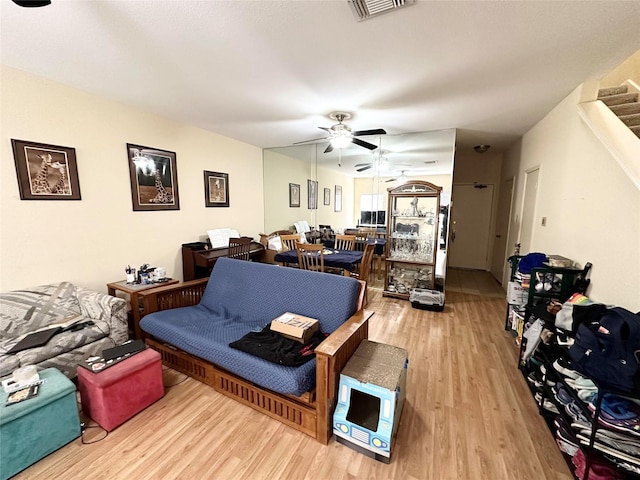 living room with a ceiling fan, light wood-type flooring, visible vents, and stairs