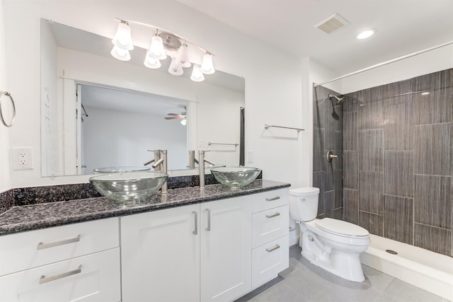 full bathroom with double vanity, tiled shower, a sink, and toilet