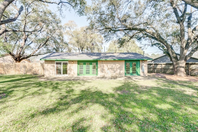 back of property featuring french doors, a fenced backyard, and a lawn