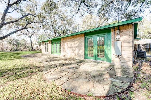 view of home's exterior featuring french doors, brick siding, a lawn, central AC, and fence