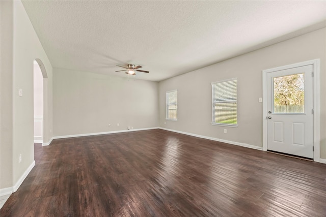 unfurnished living room featuring dark wood-type flooring, a wealth of natural light, arched walkways, and a textured ceiling