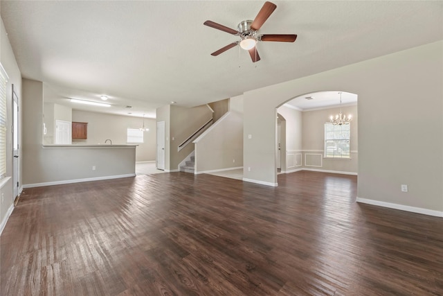 unfurnished living room featuring ceiling fan with notable chandelier, dark wood finished floors, baseboards, and stairs