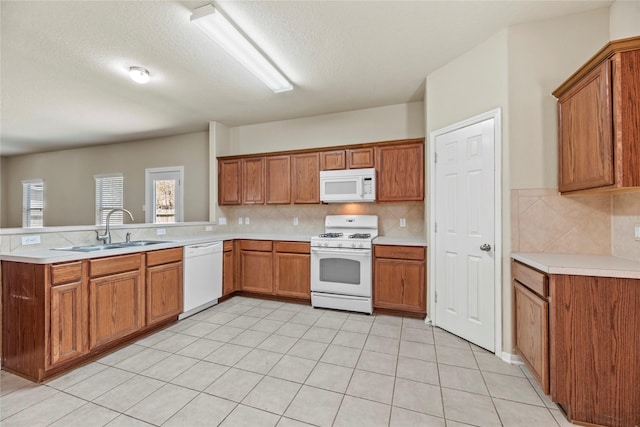 kitchen featuring a peninsula, white appliances, brown cabinets, and a sink