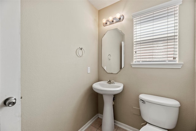 half bath with toilet, baseboards, and tile patterned floors