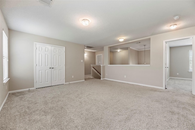 carpeted empty room featuring a textured ceiling, visible vents, and baseboards