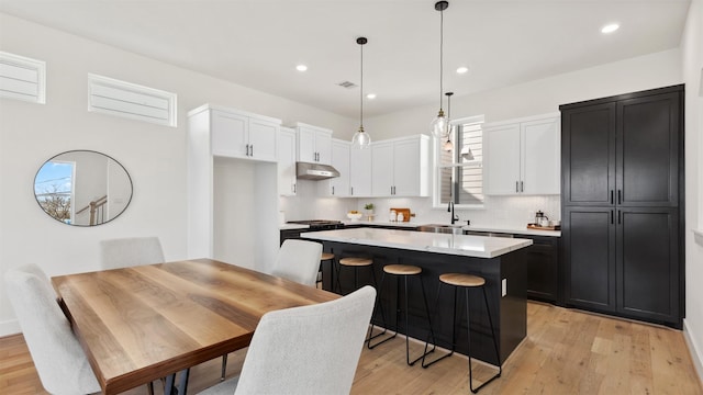 kitchen with a center island, under cabinet range hood, light countertops, white cabinets, and a sink