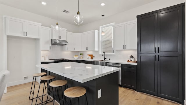 kitchen featuring visible vents, a center island, under cabinet range hood, dishwasher, and a sink