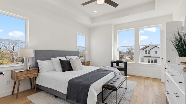 bedroom featuring light wood-type flooring, a raised ceiling, and multiple windows