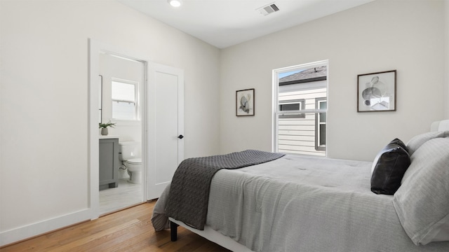 bedroom featuring light wood-type flooring, visible vents, baseboards, and connected bathroom