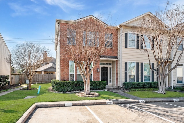 townhome / multi-family property featuring uncovered parking, a front lawn, fence, and brick siding