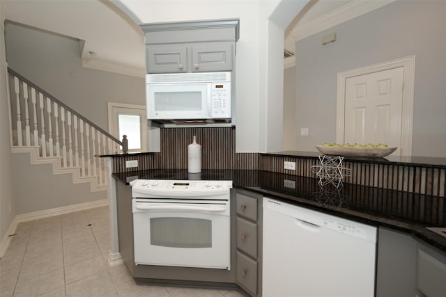 kitchen with light tile patterned floors, dark countertops, ornamental molding, white appliances, and baseboards