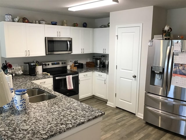 kitchen featuring stainless steel appliances, dark stone counters, dark wood-style flooring, and white cabinetry