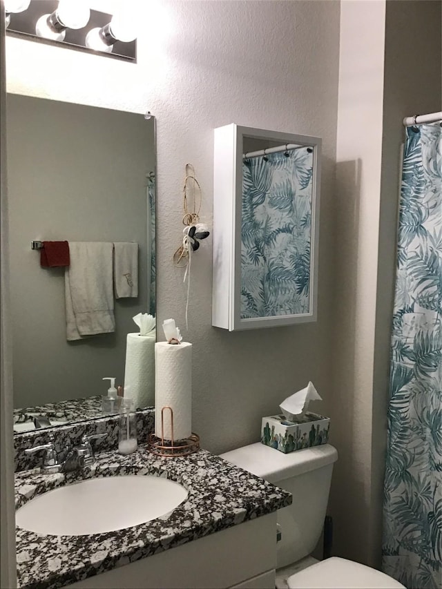 full bathroom with toilet, a textured wall, and vanity