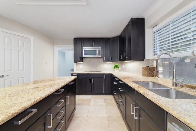 kitchen featuring appliances with stainless steel finishes, a sink, light stone countertops, backsplash, and light tile patterned flooring