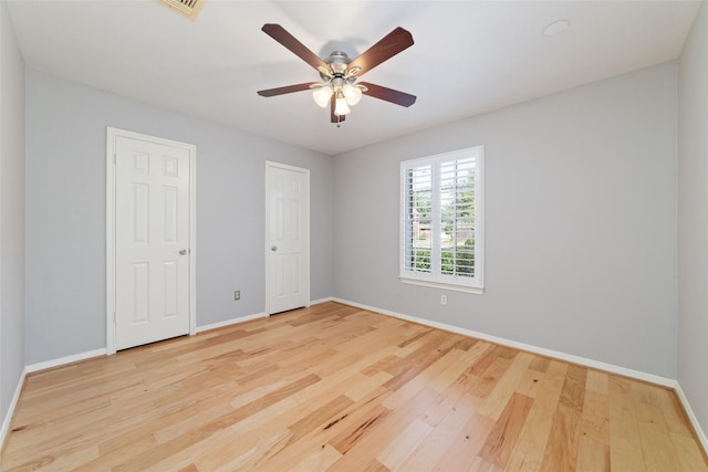 empty room with ceiling fan, visible vents, baseboards, and wood finished floors