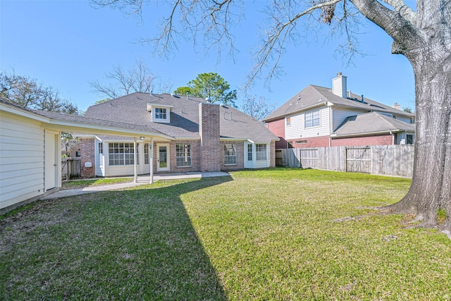 rear view of house with brick siding, a shingled roof, fence, a lawn, and a patio area