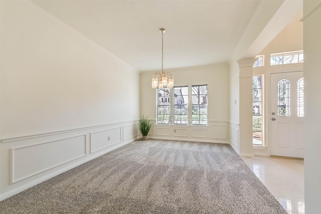 interior space featuring light carpet, an inviting chandelier, a decorative wall, and a wainscoted wall