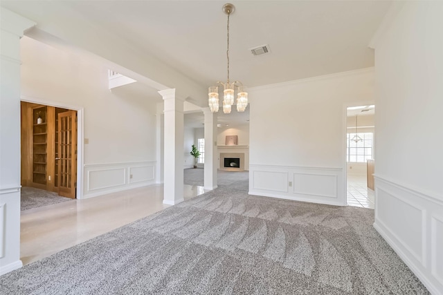 carpeted empty room with a chandelier, a decorative wall, a fireplace, visible vents, and decorative columns