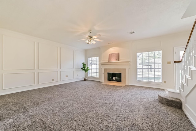 unfurnished living room featuring a decorative wall, carpet floors, a fireplace with flush hearth, visible vents, and stairs