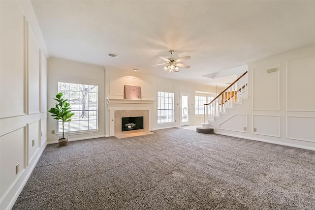 unfurnished living room featuring a decorative wall, a fireplace with flush hearth, carpet flooring, visible vents, and stairway