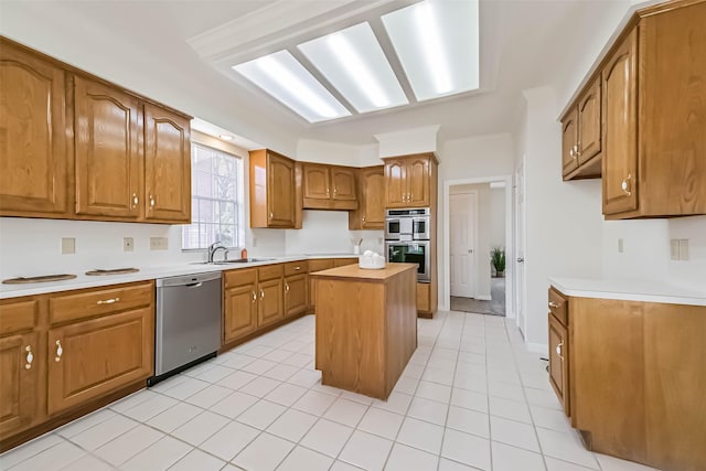 kitchen with a kitchen island, appliances with stainless steel finishes, brown cabinets, light countertops, and a sink