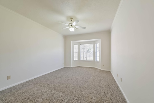 carpeted spare room with baseboards, a ceiling fan, and ornamental molding