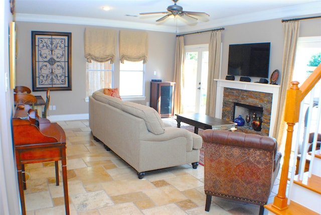 living room featuring stone tile flooring, a fireplace, crown molding, baseboards, and ceiling fan