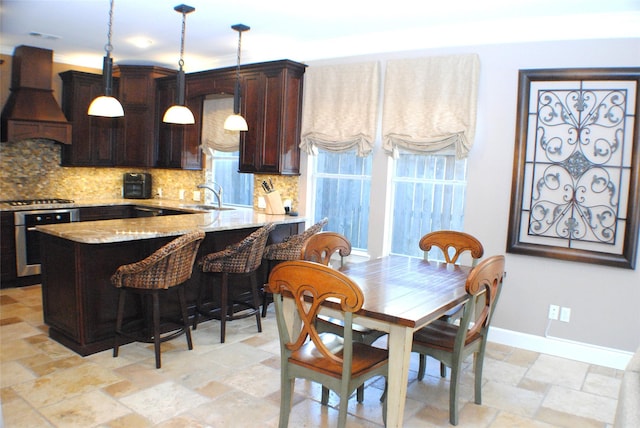 kitchen featuring premium range hood, a sink, stone tile flooring, stainless steel oven, and decorative backsplash