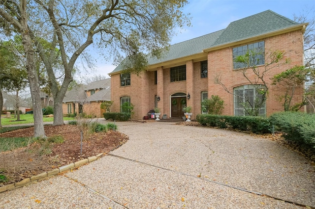 view of front of home with driveway, brick siding, and roof with shingles