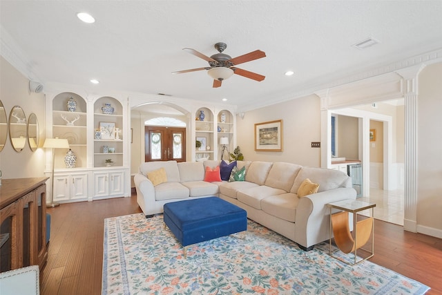 living room with ceiling fan, visible vents, built in features, wood-type flooring, and crown molding