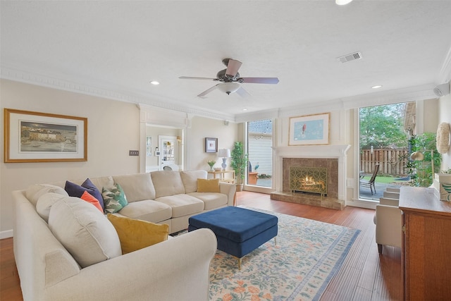 living area with visible vents, ornamental molding, a high end fireplace, a ceiling fan, and wood finished floors