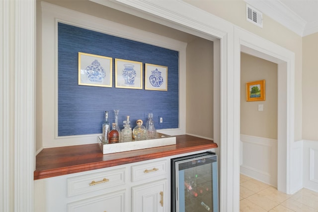 bar with wine cooler, a wainscoted wall, a dry bar, visible vents, and ornamental molding