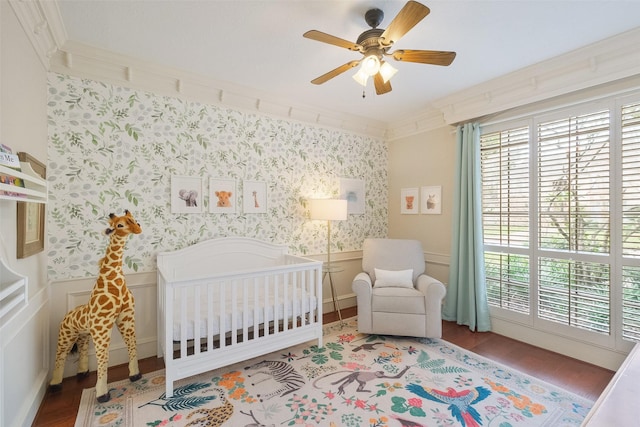 bedroom with wallpapered walls, wainscoting, ornamental molding, wood finished floors, and a nursery area