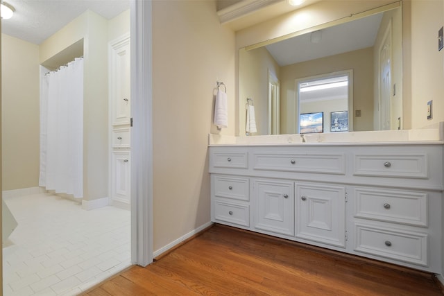 full bath with a shower with shower curtain, baseboards, wood finished floors, and vanity