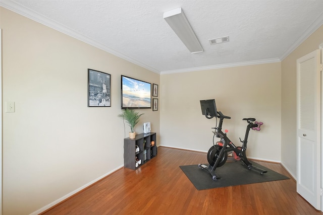 exercise area with visible vents, a textured ceiling, baseboards, and wood finished floors