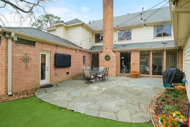 back of property featuring outdoor dining area, brick siding, a shingled roof, a chimney, and a patio area