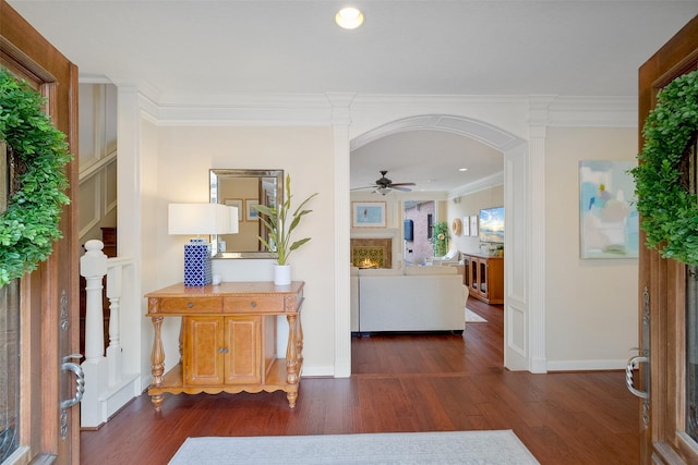 foyer featuring arched walkways, crown molding, dark wood-type flooring, a lit fireplace, and stairs