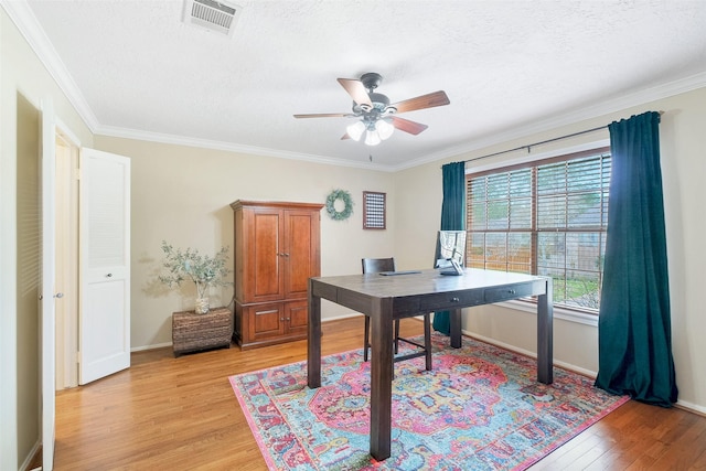 home office featuring light wood-style floors, crown molding, visible vents, and a ceiling fan