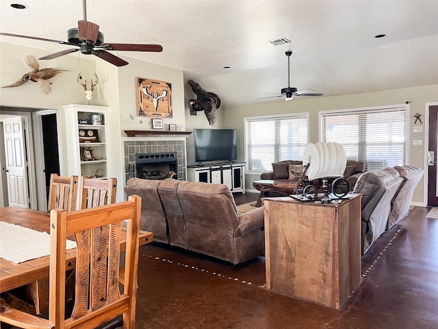 living area with visible vents, a textured ceiling, lofted ceiling, ceiling fan, and a tile fireplace