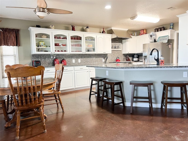 kitchen featuring a kitchen breakfast bar, stainless steel appliances, wall chimney exhaust hood, white cabinets, and glass insert cabinets