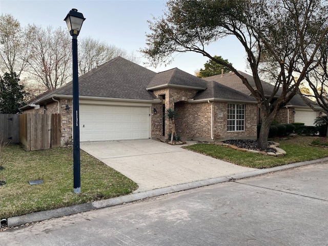 ranch-style home featuring fence, roof with shingles, concrete driveway, a front yard, and an attached garage