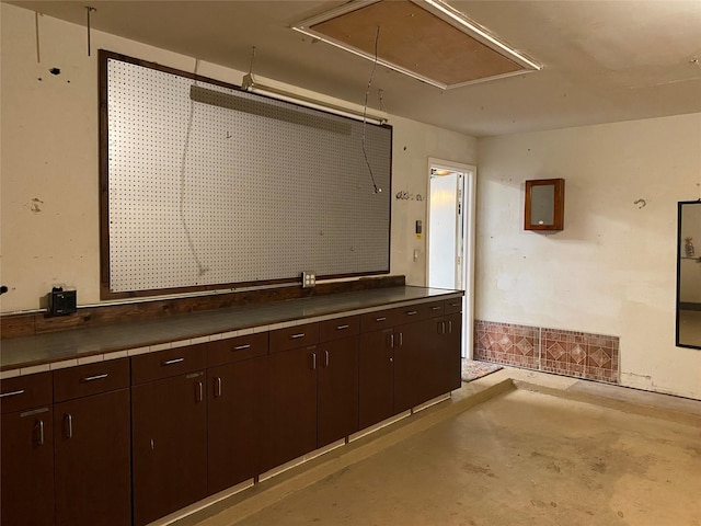 interior space with tile countertops, dark brown cabinetry, and unfinished concrete floors