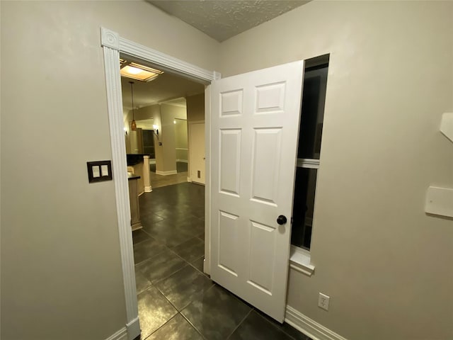 hall featuring dark tile patterned flooring, baseboards, and a textured ceiling