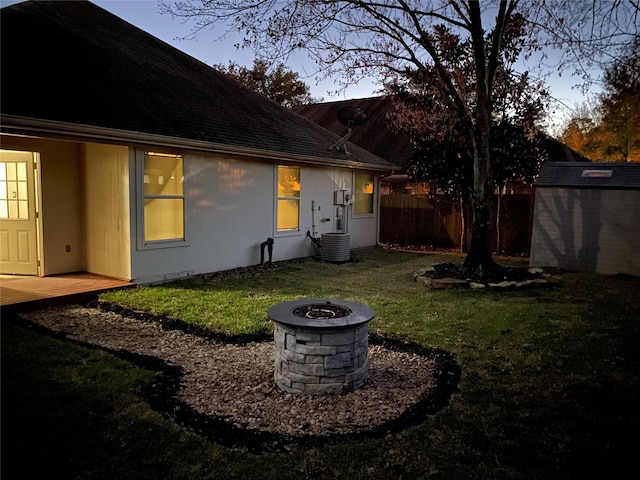 rear view of house featuring a lawn, a fire pit, an outdoor structure, and fence