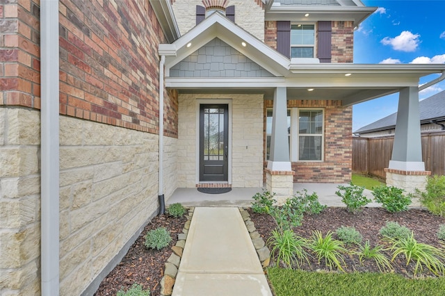 doorway to property featuring covered porch, brick siding, and fence