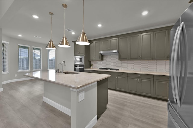 kitchen with stainless steel appliances, decorative backsplash, a kitchen island with sink, a sink, and under cabinet range hood