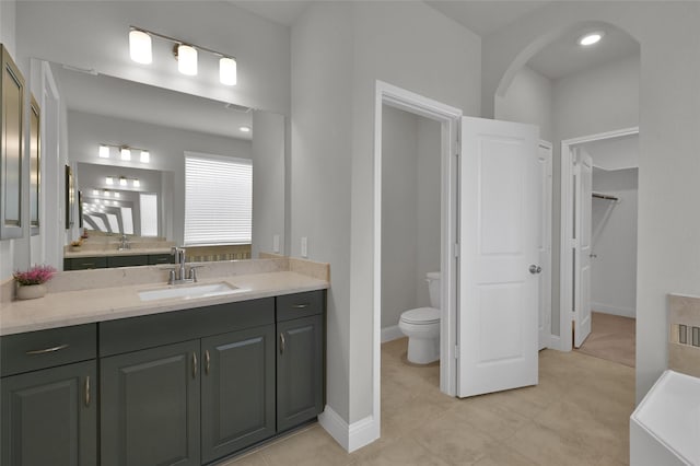 full bath with a walk in closet, toilet, vanity, baseboards, and tile patterned floors